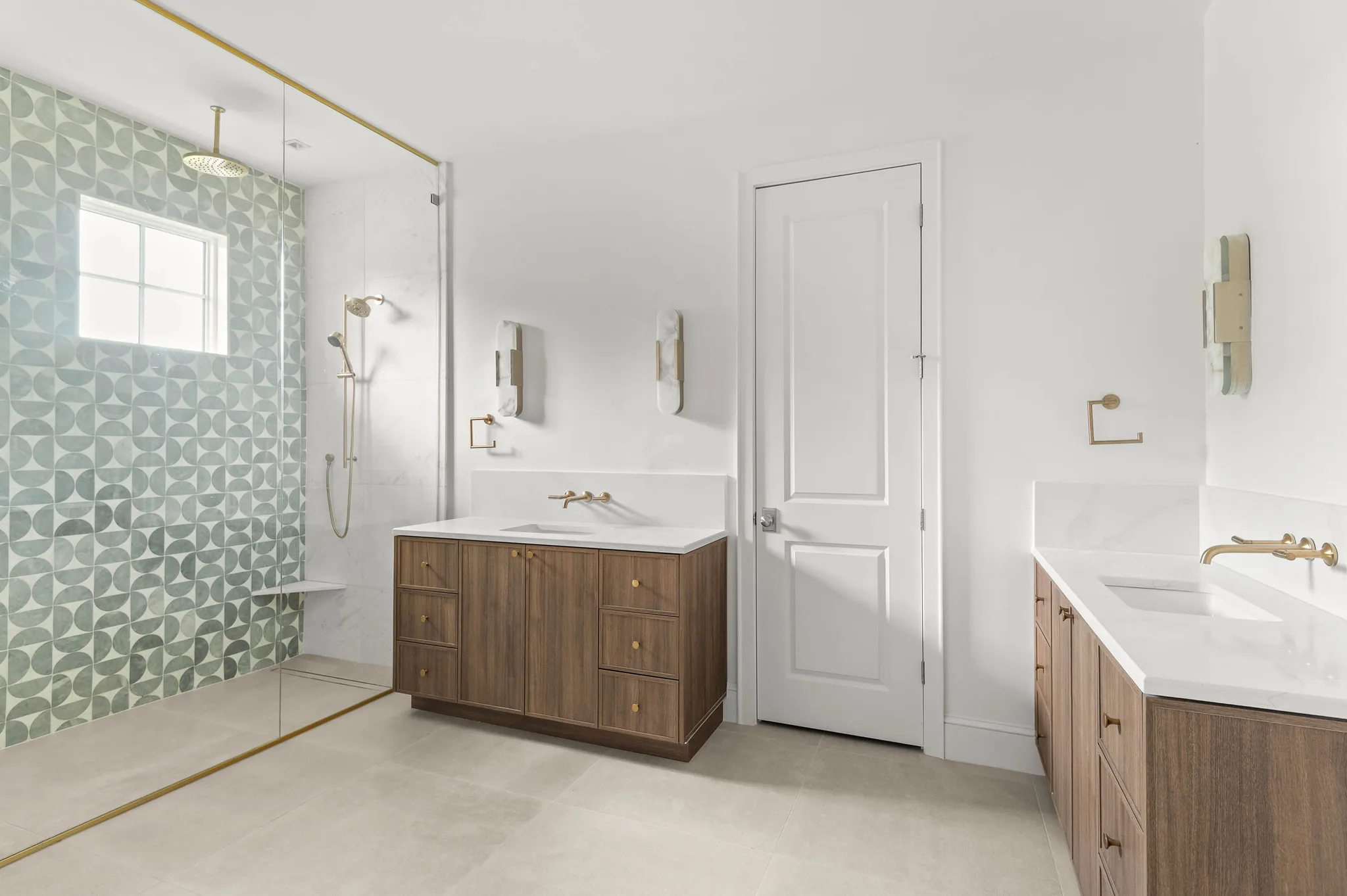 Primary bathroom with twin walnut vanities, brass fittings, and glass shower